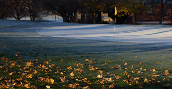 Frozen golf course. autumn leaves This landscape photograph shows a frozen golf course on a winter morning in Tapton Park, Chesterfield, United Kingdom. The ground is covered with a layer of frost, and autumn leaves are scattered across the grass in the foreground, highlighting the seasonal transition. The image captures the nature of the park with its mature trees providing a scenic background, while the golf flag stands out as the main feature on the frosty course. The low morning sunlight casts long shadows from the trees, enhancing the wintry atmosphere typical of this time of year.